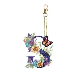 Llave de oro con cadena dorada unida a un 'Llavero Pintura de Diamantes DIY de la A-Z colgante de llavero', presentando una letra S decorada con mariposa de colores, flores multicolores y perlas decorativas sobre un fondo blanco.