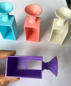 Objetos con embudos en azul, rosa y blanco sobre una superficie blanca, y un objeto púrpura sostenido por una mano, utilizados para Embudo de Diamantes Diamond