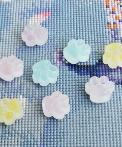 Superficie con patrón de cuadrícula mostrando figuras de huellas de pata en colores pastel como rosa, azul y amarillo, reflejando luz brillante en un diseño de Cover Minder Diamond Painting ​Luminous Footprint.