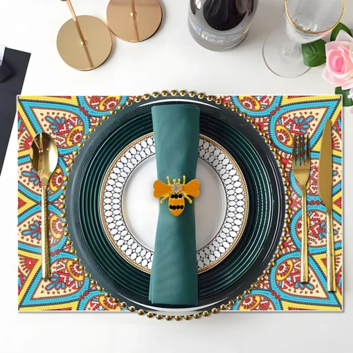 Un elegante mantel con un patrón colorido presenta un plato negro grande con borde dorado, un plato blanco con diseño circular, una servilleta verde oscuro adornada con un sujetador de servilleta en forma de abeja, acompañado de una cuchara y un tenedor dorados, un vaso con borde dorado, una botella de vino, una rosa artificial rosa y candelabros dorados, todo sobre un Tapete Antideslizante Mandala Diamond Painting.