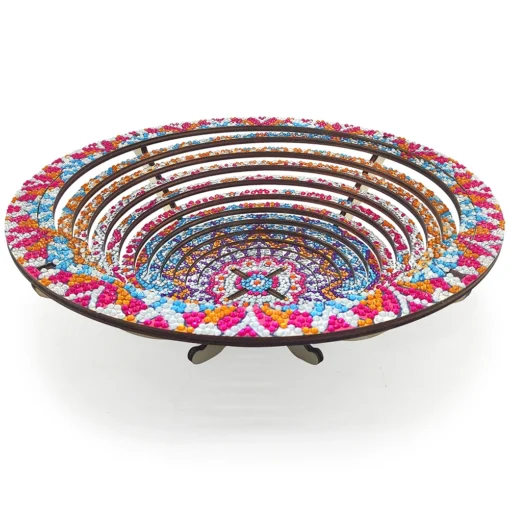 Plato Decorativo Cocina Punto de Diamantes con diseño circular de círculos concéntricos, decorado con cuentas pequeñas en colores brillantes como azul, rosa, naranja y blanco, con motivos geométricos sobre fondo blanco y una base de soporte.