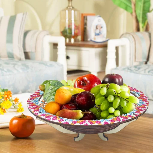 Frutero lleno de uvas verdes, manzanas y duraznos en un "Plato Decorativo Cocina Punto de Diamantes" sobre una mesa de madera en sala con sillones claros y flores naranjas en un jarrón; fondo borroso.