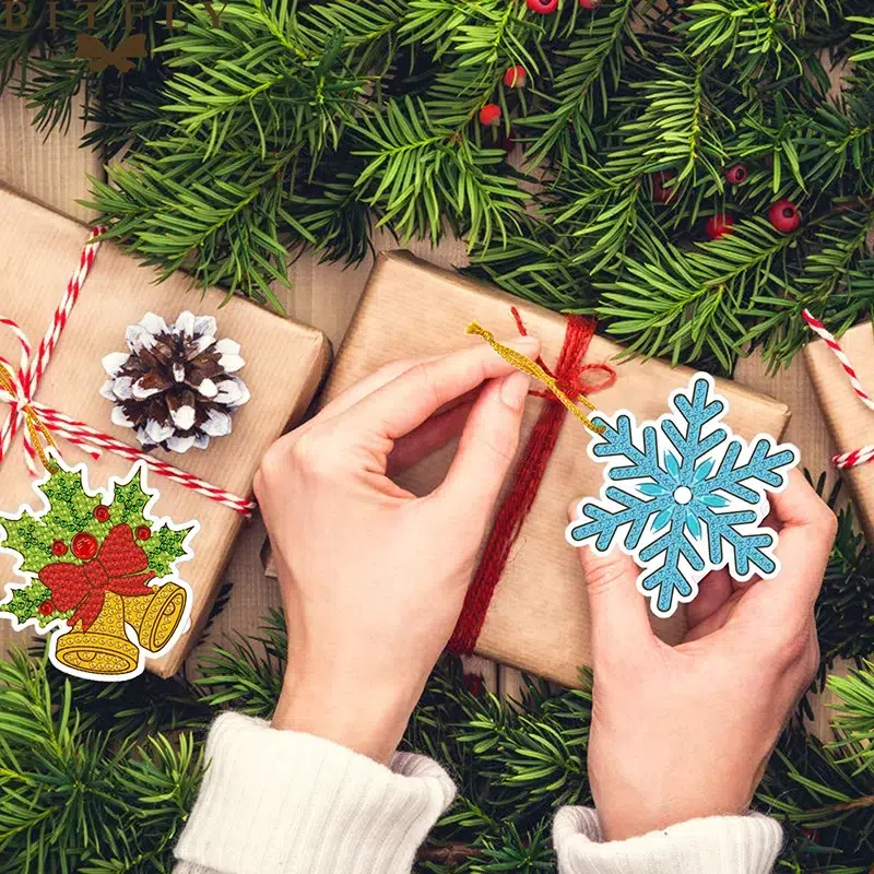 Manos atando un regalo envuelto en papel kraft con cuerda roja entre ramas de pino y adornos navideños, Decoración Santa Claus Navidad Bordado de Luz